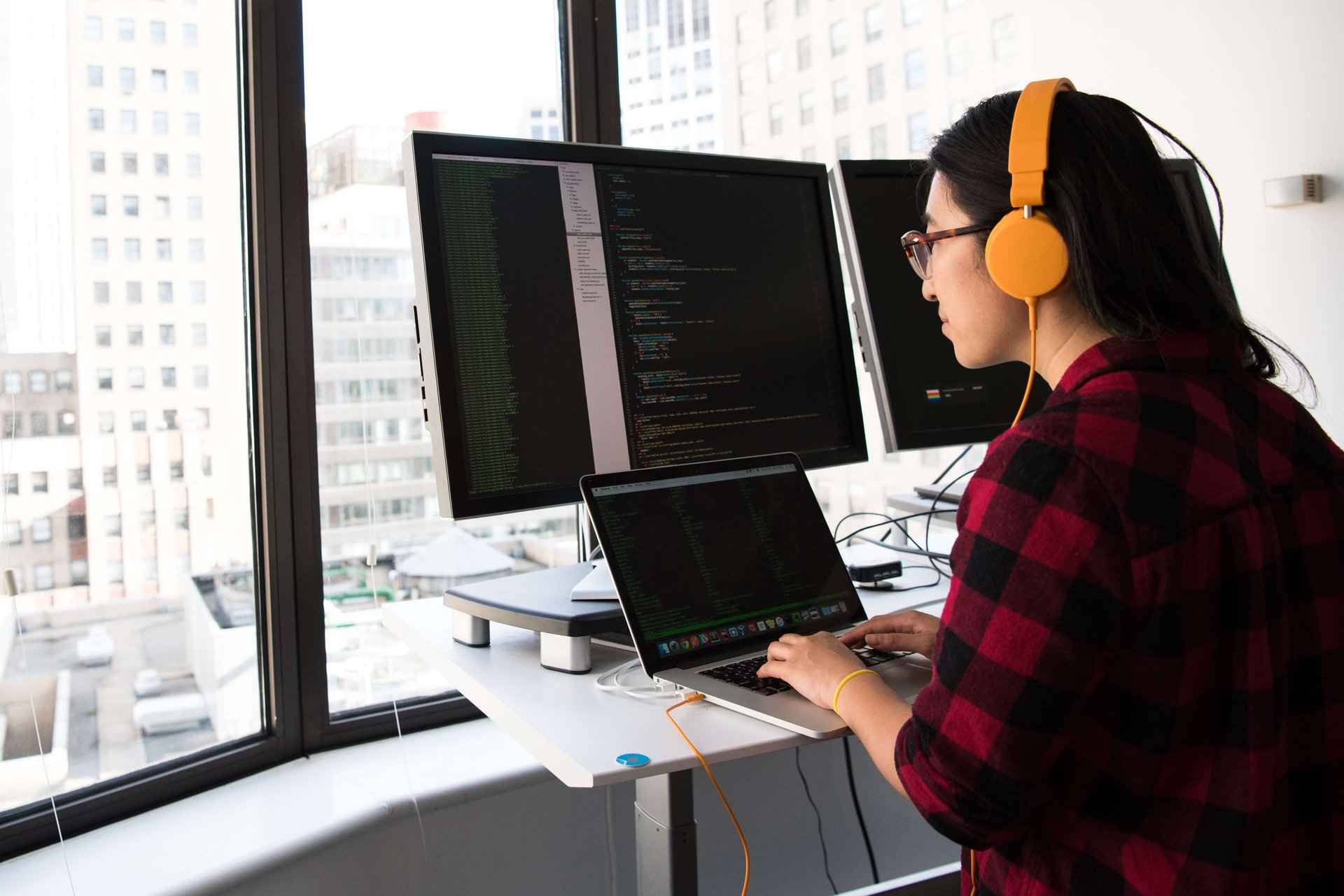 female developer with yellow headphones with three screens with code