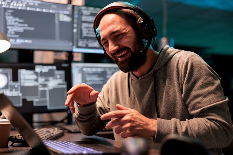 smiling developer with earphones and screens with code in the background