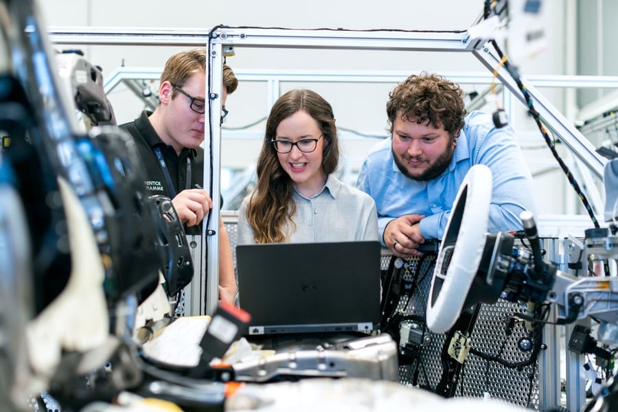 two males and one female engineers collaborate with computers and beginning of a car